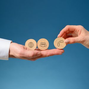 Female hand placing three wooden cut circles with contact and communication icons on them on a businessmans hand.